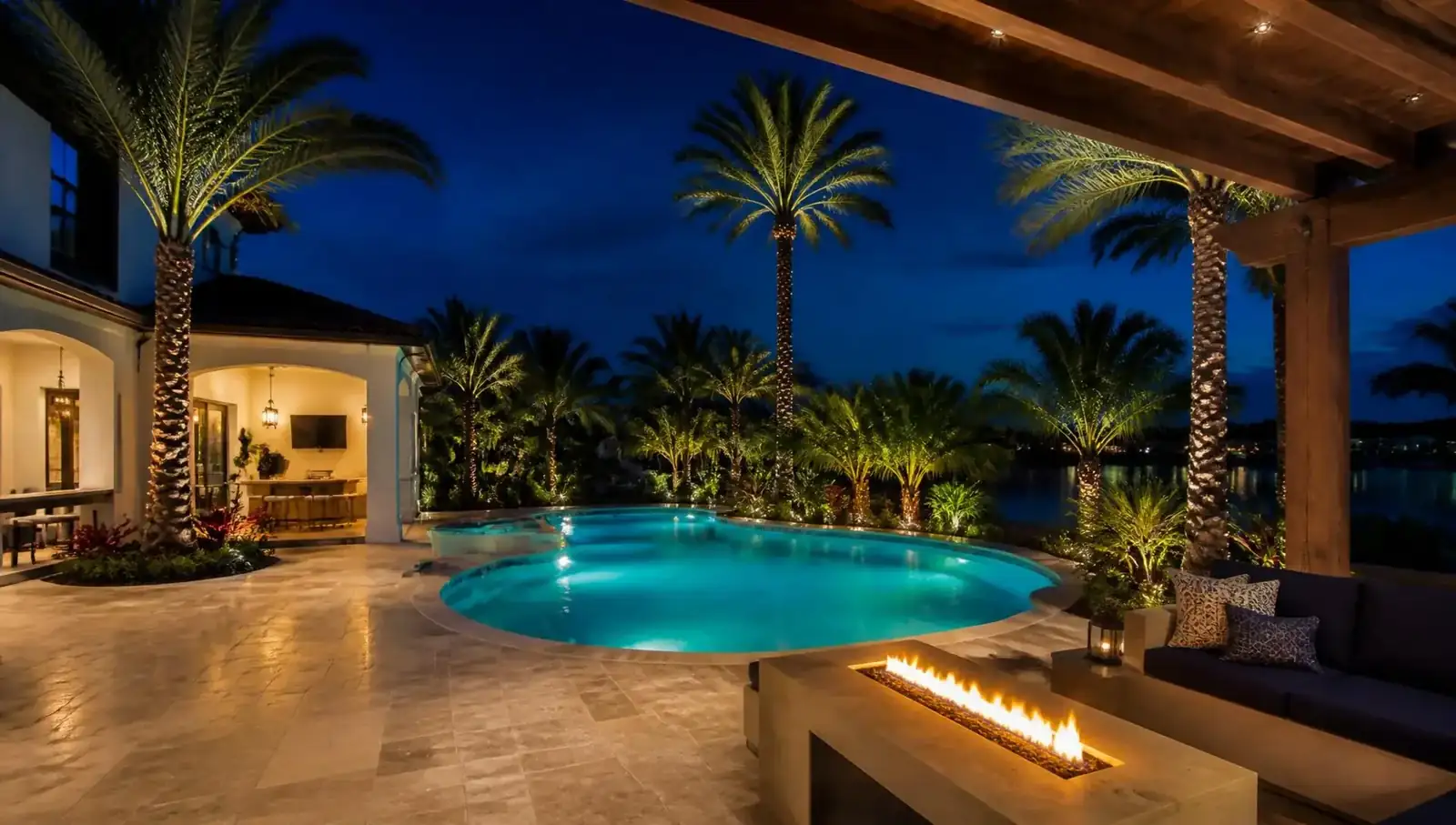 Luxury St. Augustine backyard at blue hour with a lit pool, palm trees, pergola and fire feature